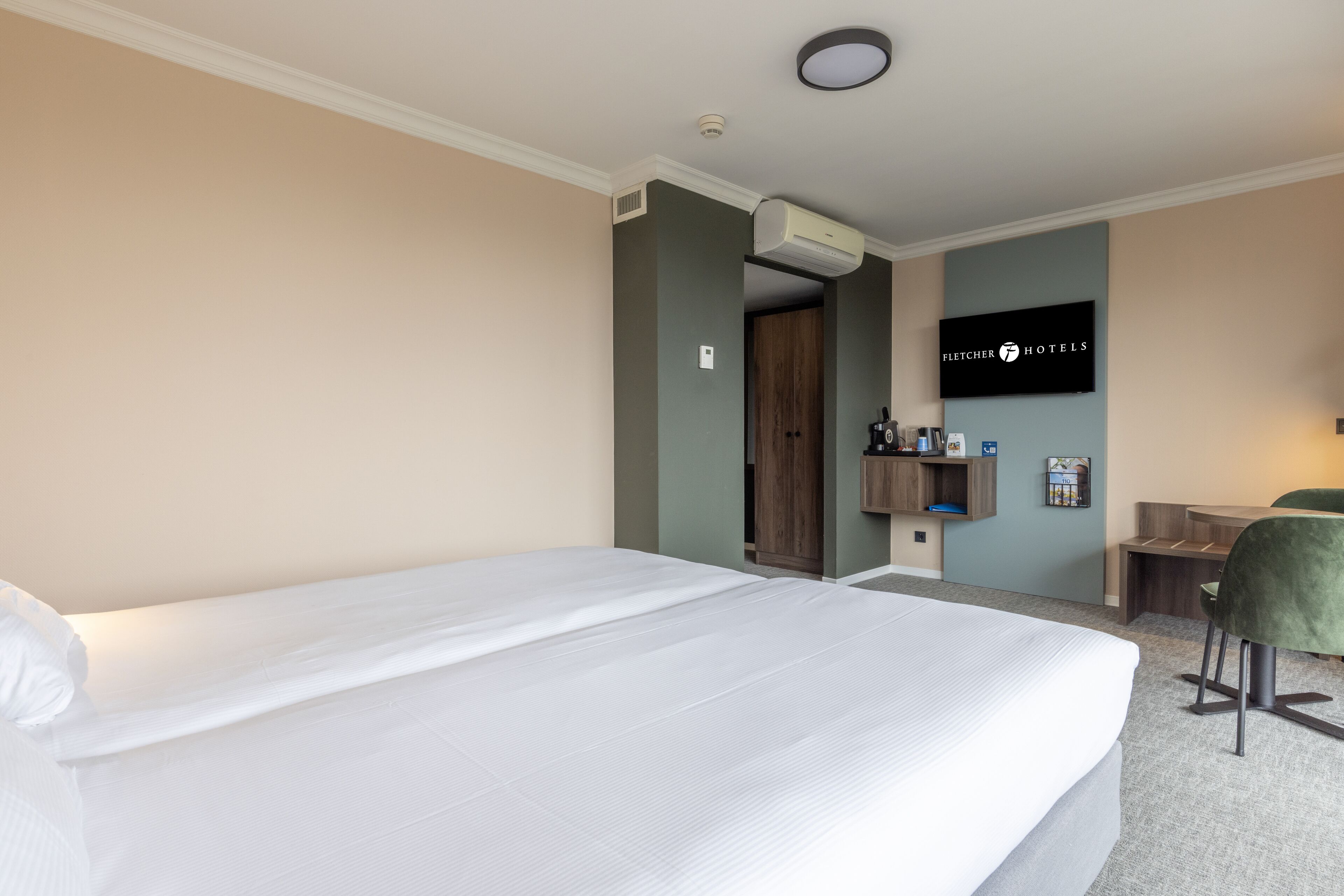 Une chambre d’hôtel avec un grand lit, un bureau avec une chaise, un téléviseur fixé au mur et un appareil de climatisation.