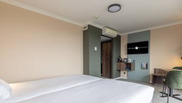 Une chambre d’hôtel avec un grand lit, un bureau avec une chaise, un téléviseur fixé au mur et un appareil de climatisation.