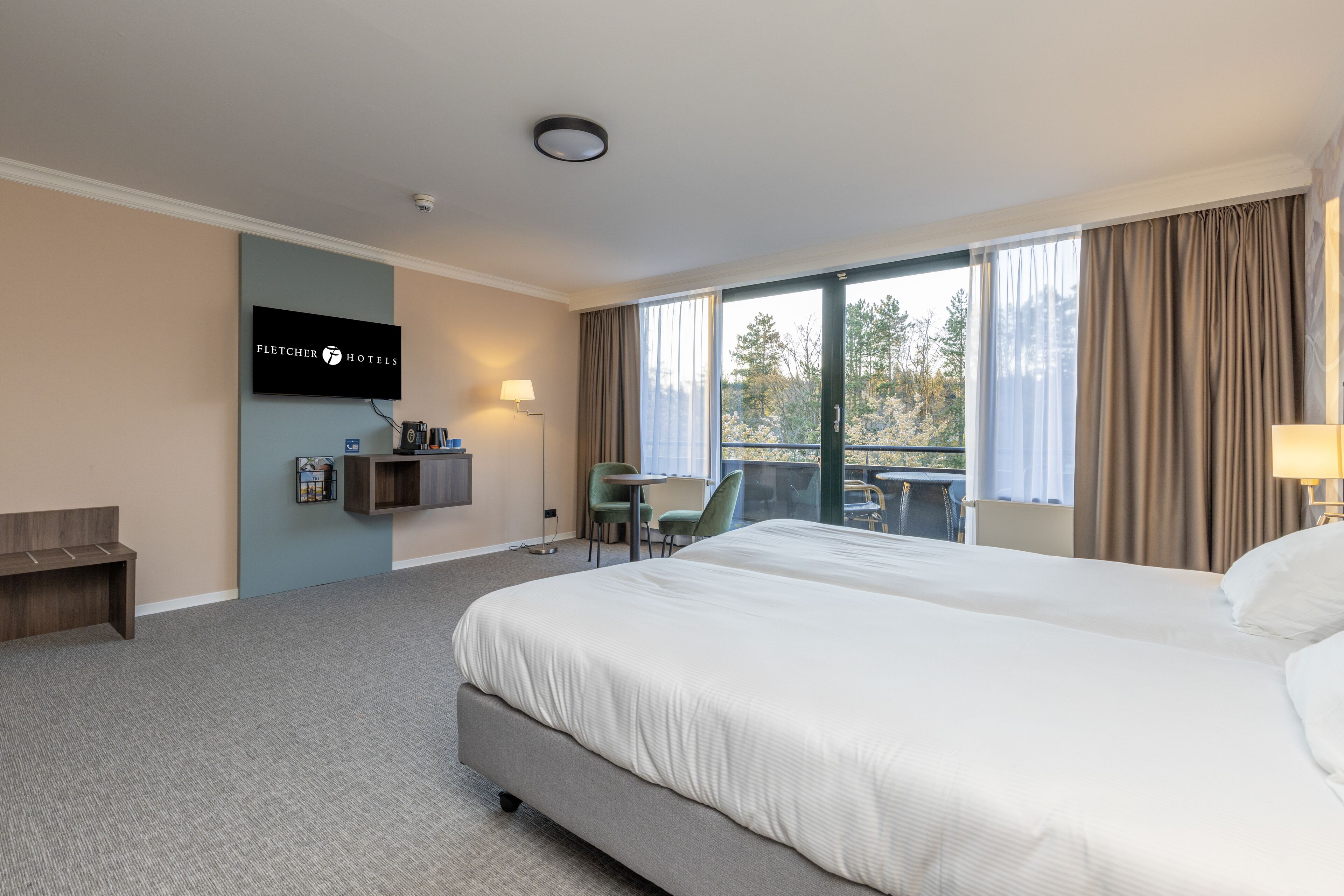 Een hotelkamer met een groot bed, een bureau, een stoel en een aan de muur bevestigde televisie.