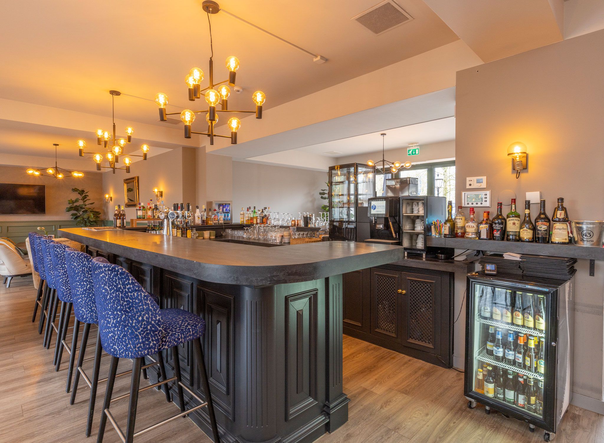 Zona de bar con mostrador, taburetes y refrigerador lleno de bebidas.