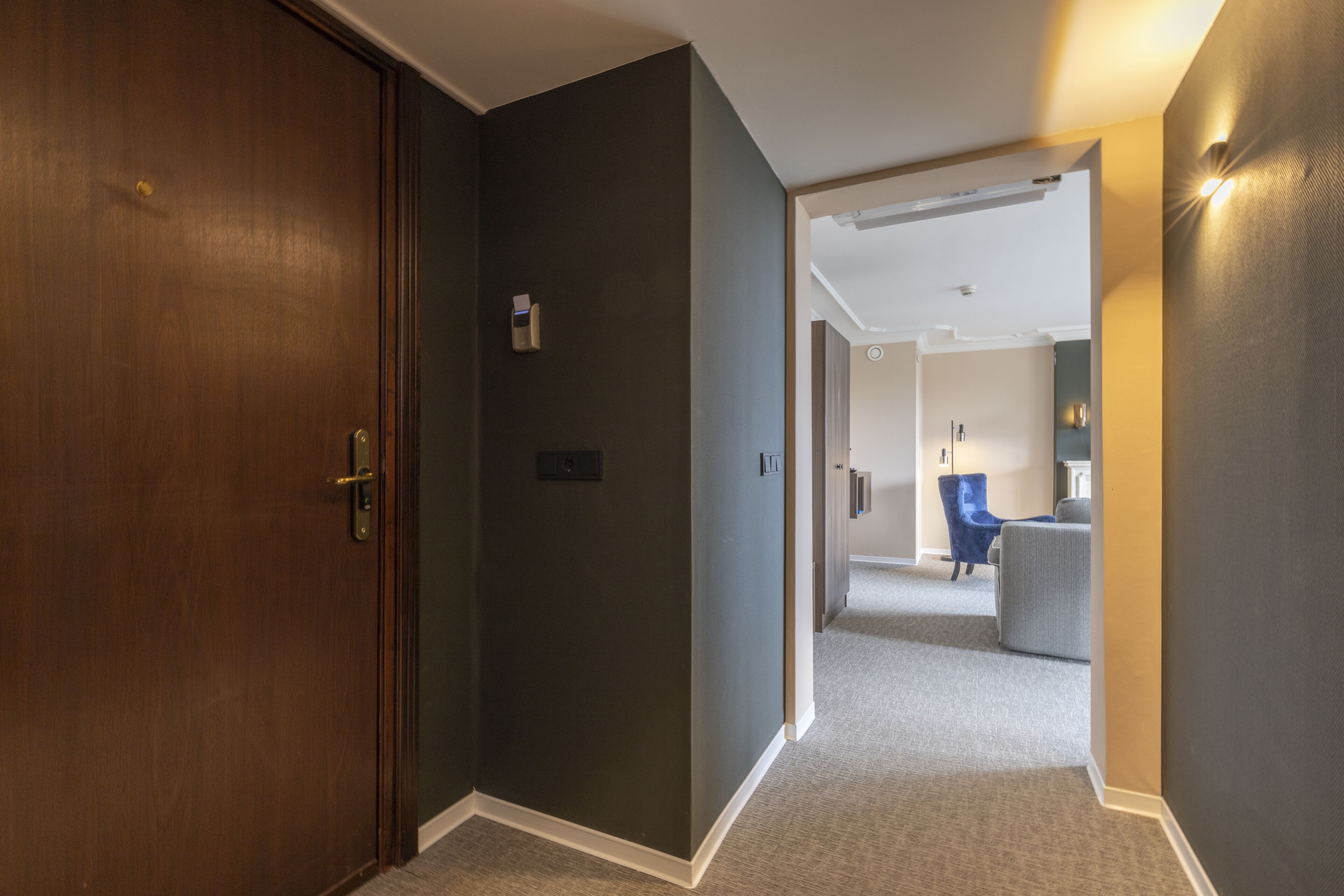 A hallway with a wooden door, a light switch, and a wall-mounted light fixture.