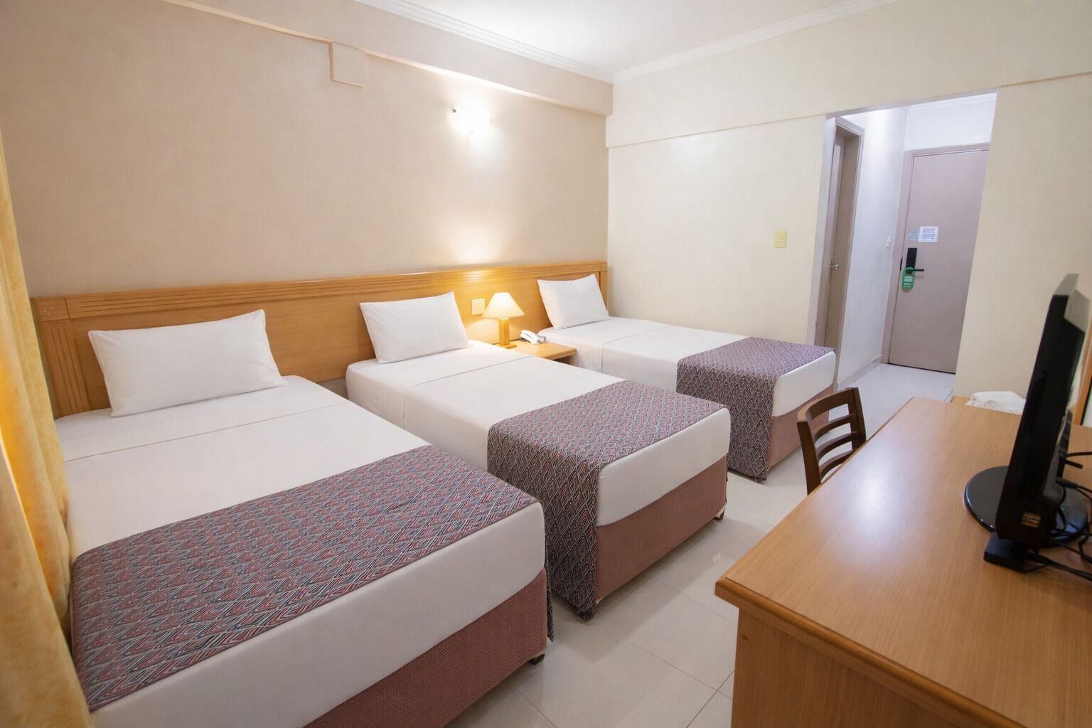 A hotel room with three beds, a desk with a computer, and a door leading to another room.