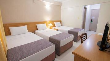 A hotel room with three beds, a desk with a computer, and a door leading to another room.