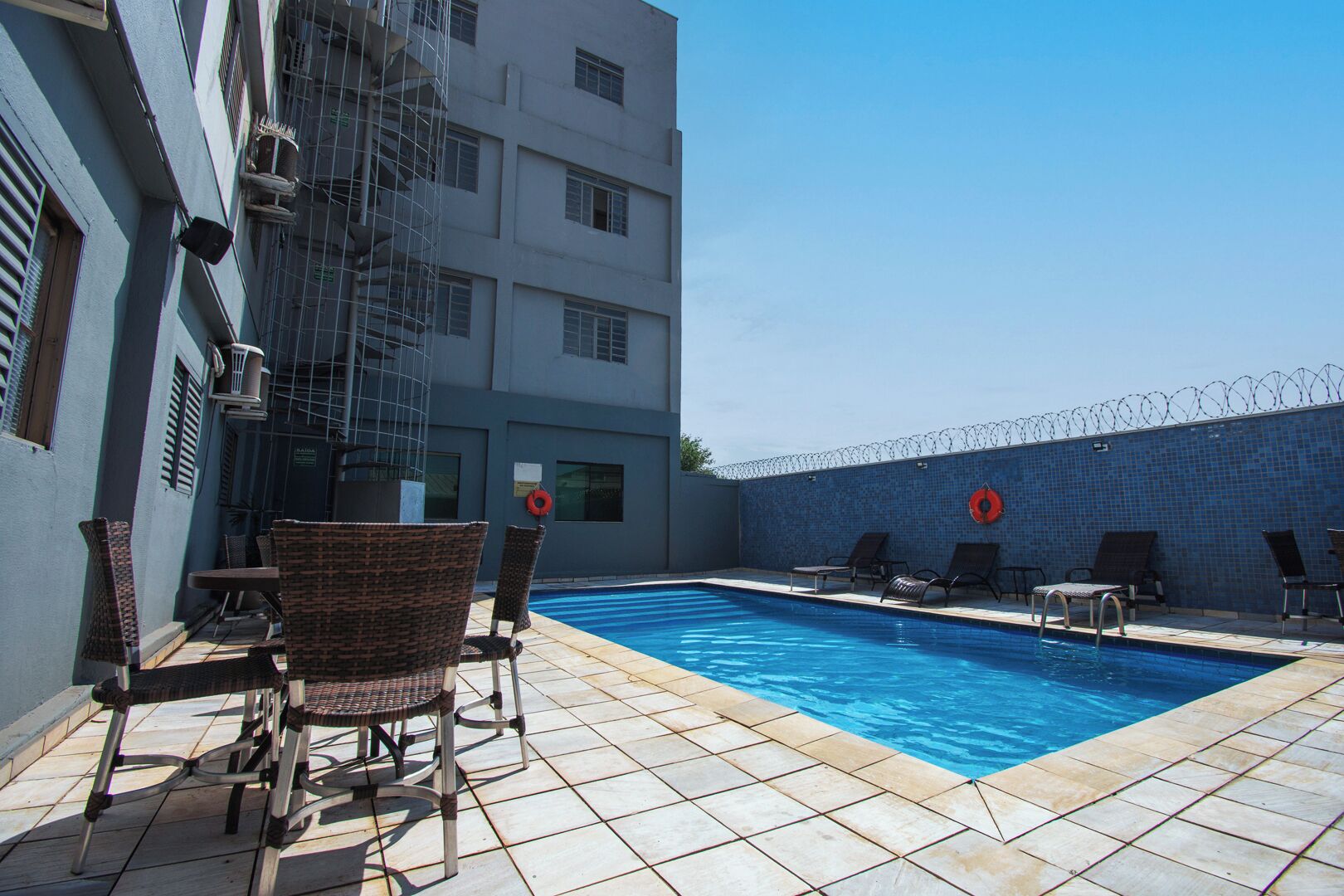 A swimming pool with lounge chairs and a barbed wire fence.