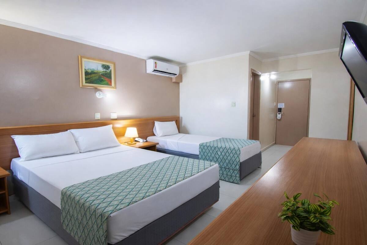 Ein Hotelzimmer mit zwei Betten, einem Holztisch, einem Fernseher und einem Bild an der Wand.