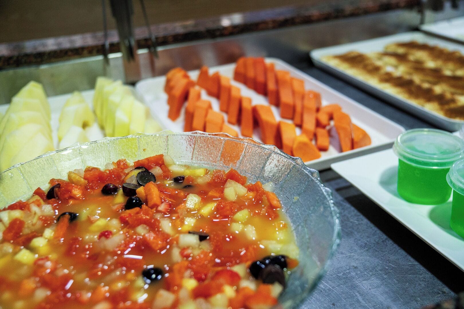 Buffet com diversos pratos, incluindo uma refeição vegetariana, cenouras fatiadas e uma sobremesa verde.