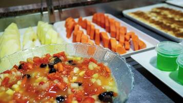 Buffet com diversos pratos, incluindo uma refeição vegetariana, cenouras fatiadas e uma sobremesa verde.