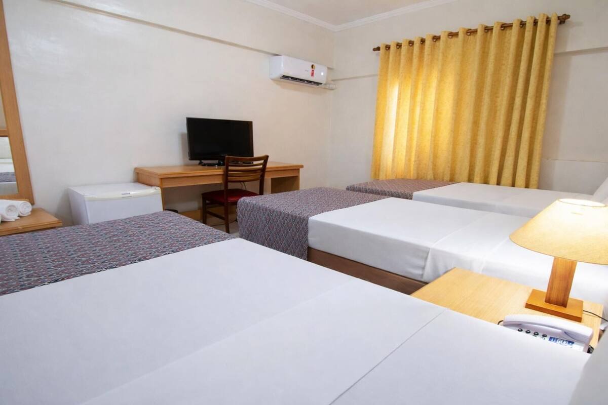 Ein Hotelzimmer mit zwei Betten, einem Schreibtisch, einem Stuhl, einem Fernseher, einer Klimaanlage und einer Lampe.