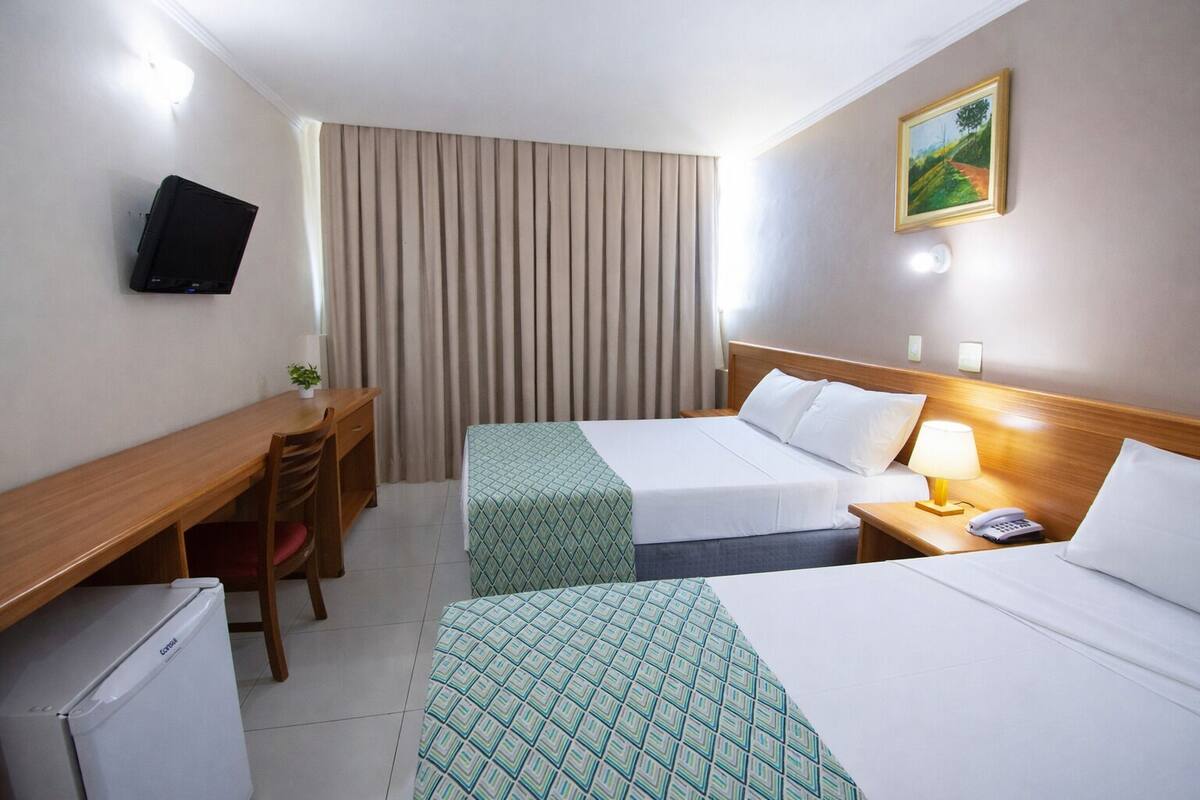 Ein Hotelzimmer mit zwei Betten, einem Schreibtisch, einem Sessel, einem Fernseher und einem Bild an der Wand.