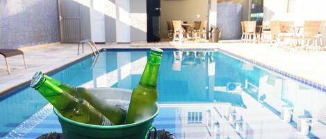 A poolside area with a green bucket containing two bottles, lounge chairs, and a glass table.