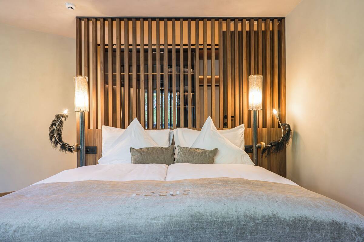 Une chambre d’hôtel moderne avec un grand lit, des lambris en bois en arrière-plan et deux lampes fixées au mur.