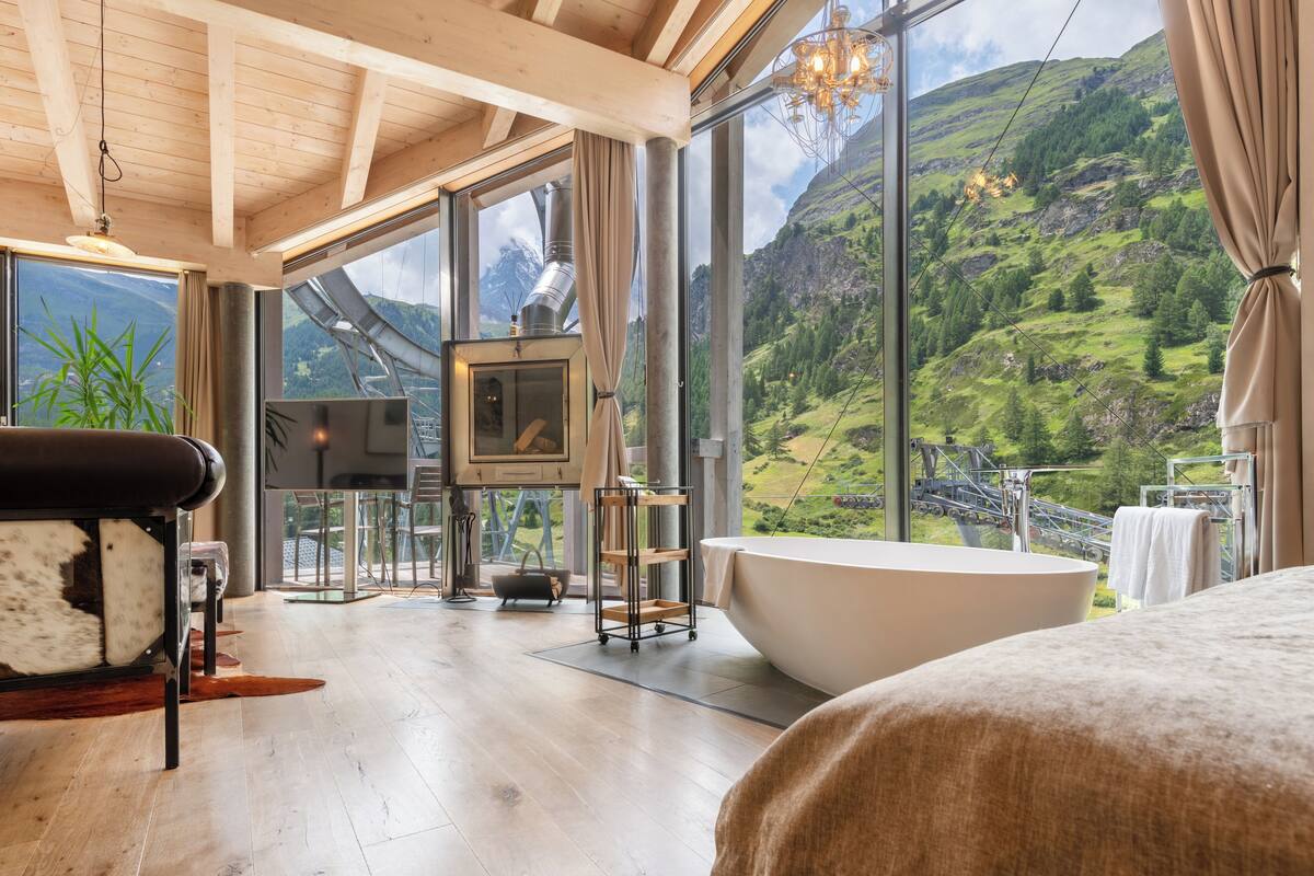 Une salle de bain moderne avec une grande baignoire, un plancher en bois et une vue sur un paysage montagneux grâce à de grandes fenêtres.
