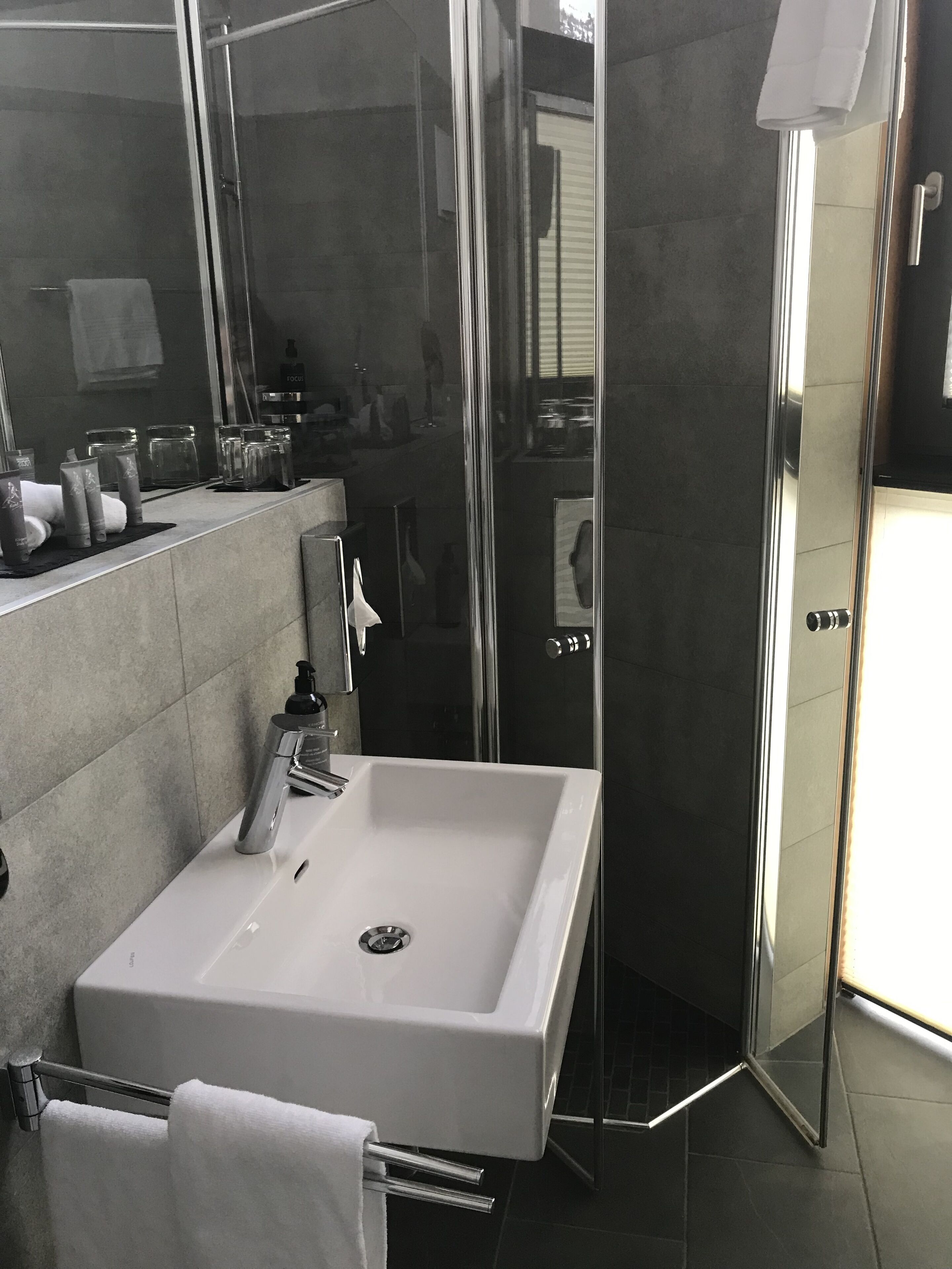 Um banheiro moderno com uma pia grande e branca, box de vidro e um espelho refletindo o ambiente.