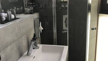 Um banheiro moderno com uma pia grande e branca, box de vidro e um espelho refletindo o ambiente.