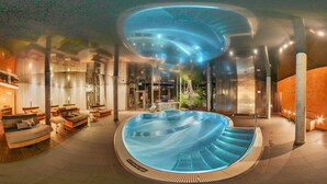 Un espace piscine intérieur moderne, doté d’un design incurvé, de coins salon et d’un bar.