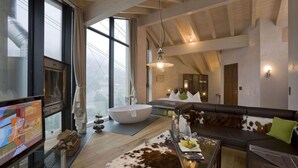 Un salon moderne doté d’un grand téléviseur à écran plat, d’un plafond en bois, d’une grande fenêtre, d’une baignoire blanche, d’un canapé en cuir et d’une table basse en verre.