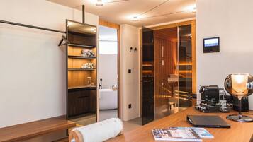 A modern hotel room with a wooden desk, a laptop, a coffee machine, and a large mirror.