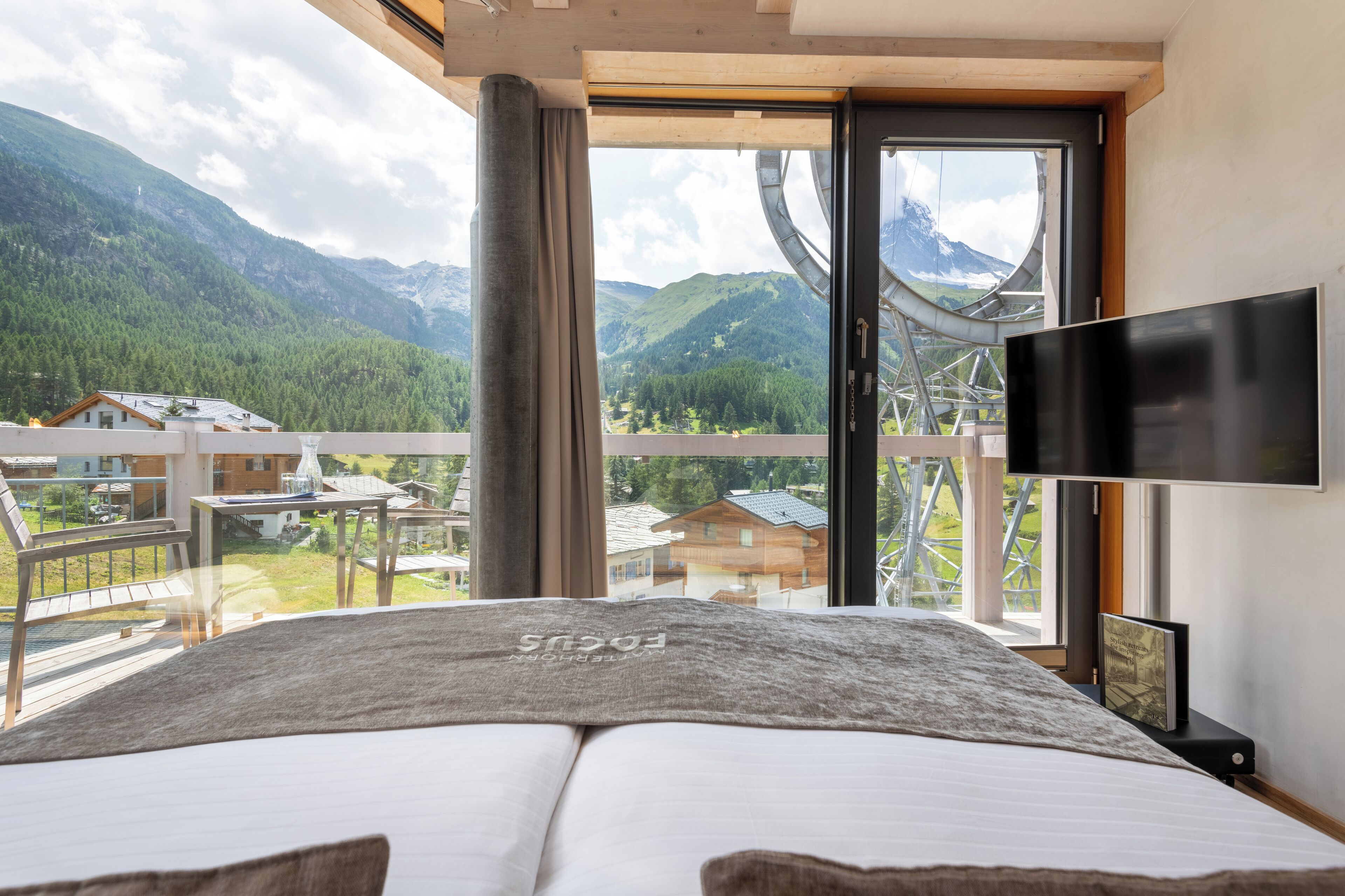 Ein Schlafzimmer mit Bett, Fernseher und einem Balkon mit Bergblick.