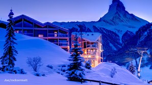 Un bâtiment moderne qui abrite une station de ski, avec plusieurs étages et de grandes fenêtres, entouré de montagnes enneigées et d'un télésiège.