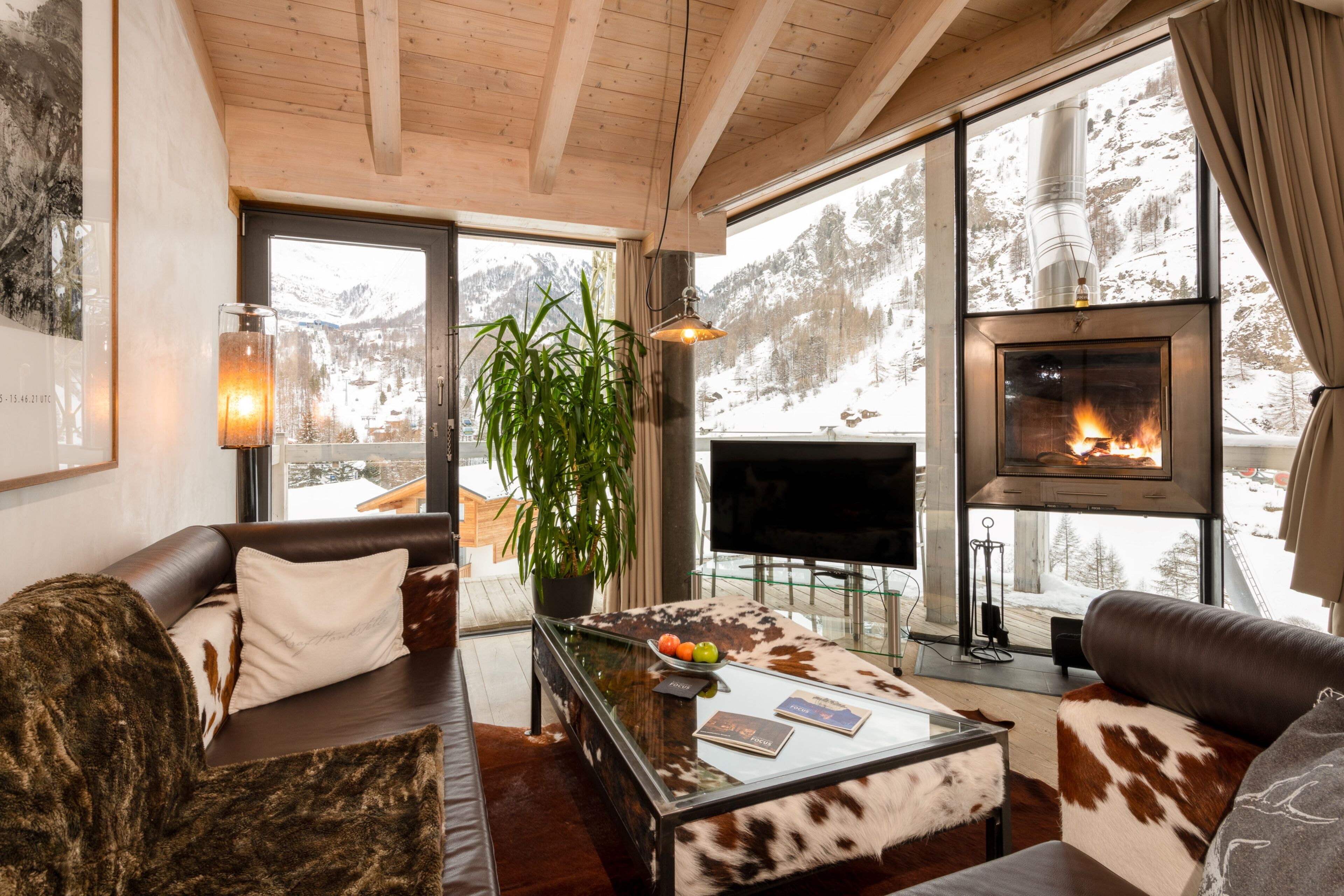 A cozy living room with a fireplace, leather sofas, a glass coffee table, and a large window offering a mountain view.