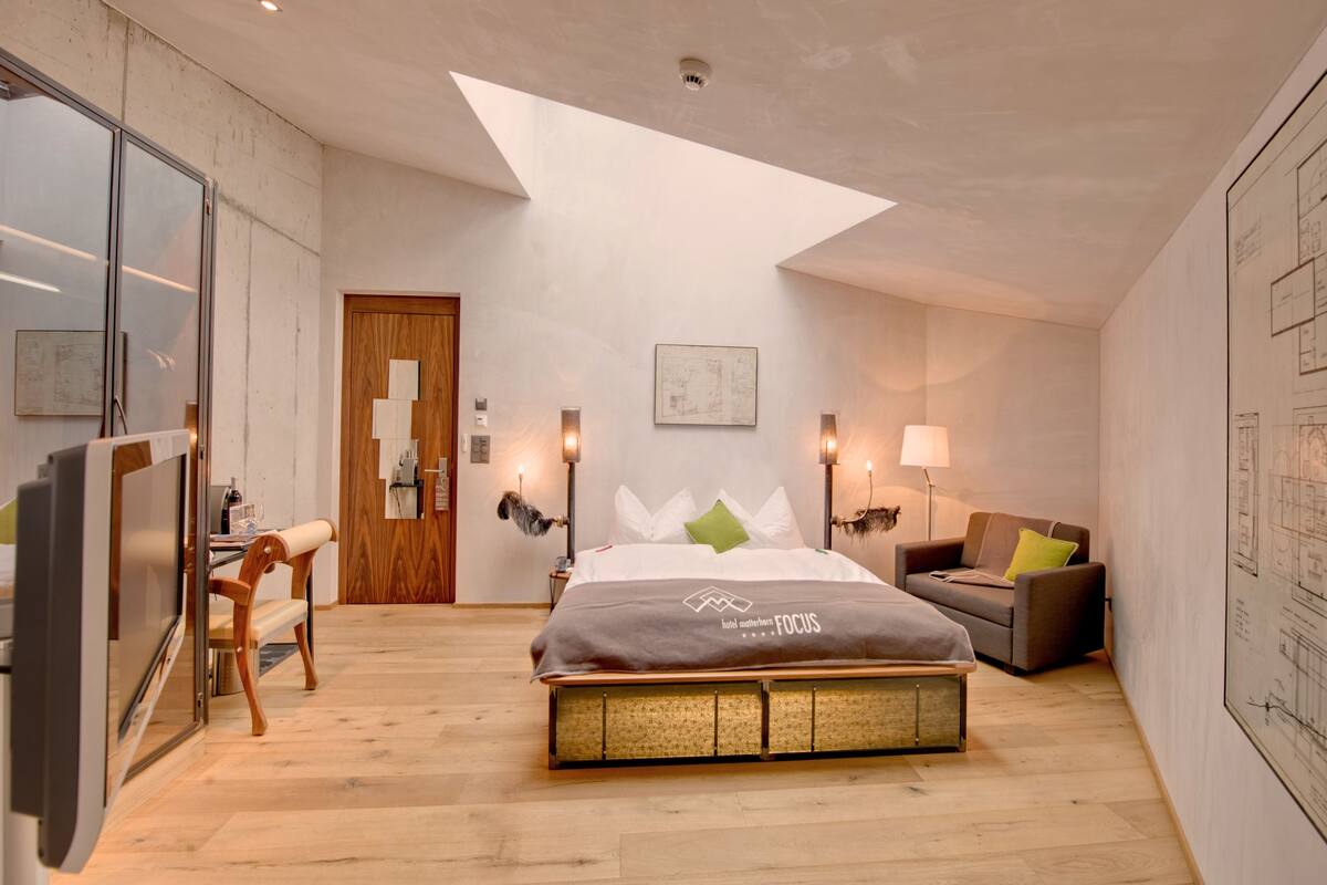 Une chambre d’hôtel moderne avec un grand lit, un bureau et une chaise. On y trouve une porte en bois et un mur orné d’une carte.