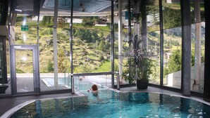 Une piscine intérieure dotée d’un mur en verre qui offre une vue sur un paysage montagneux.