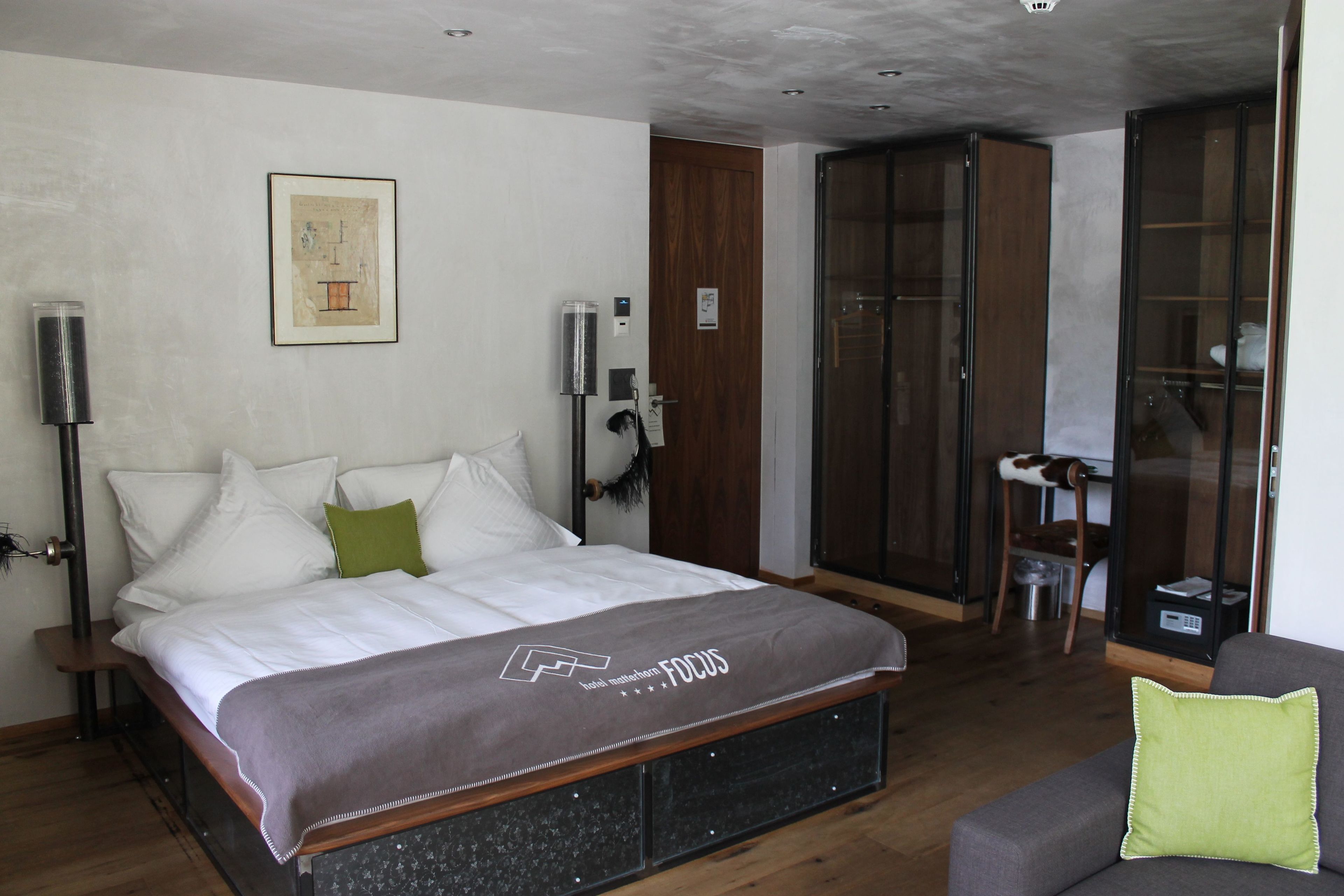 A modern bedroom with a large bed, a grey sofa, and a wooden wardrobe.
