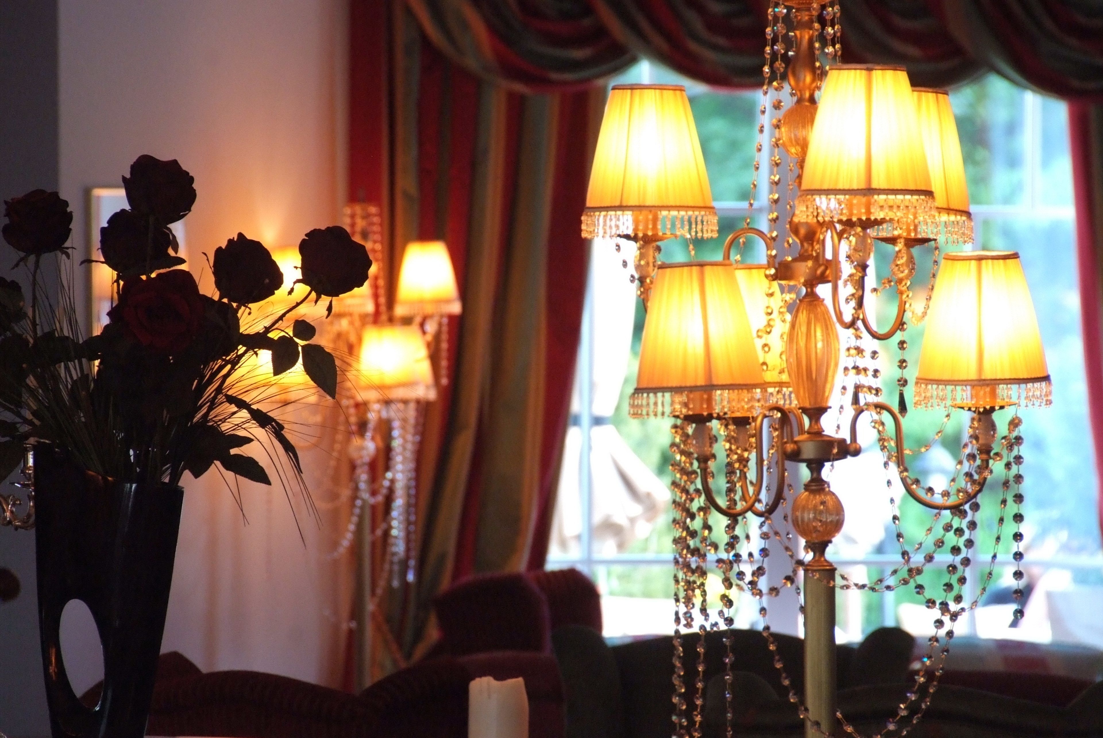 A chandelier with multiple lamps, a vase with roses, and a window with curtains in the background.