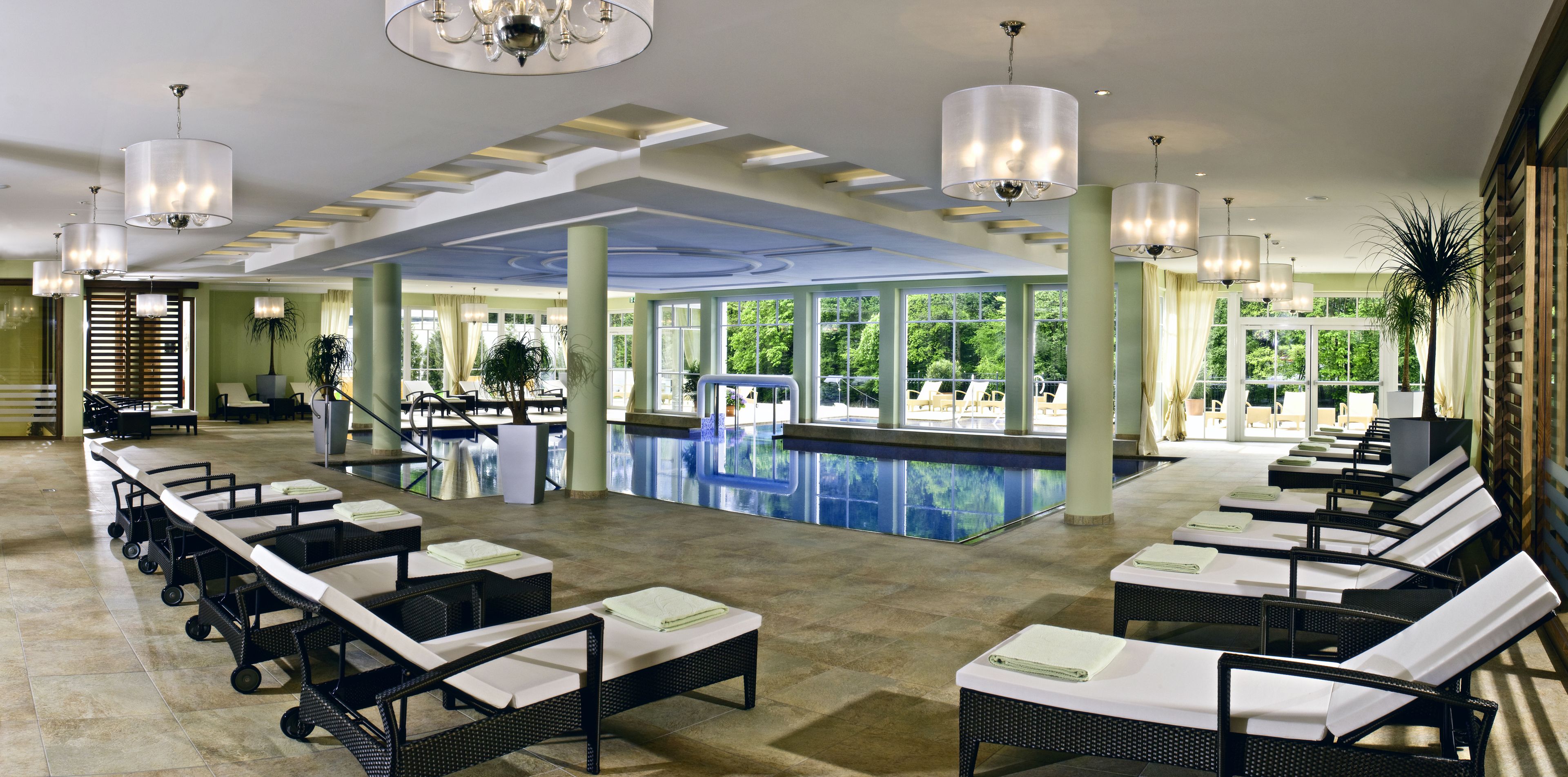 Un vestíbulo de hotel con piscina, sillones de descanso y zona de comedor.