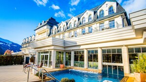 A large, multi-story hotel with a swimming pool, outdoor seating, and a mountain backdrop. - Grandhotel Lienz (Lienz)