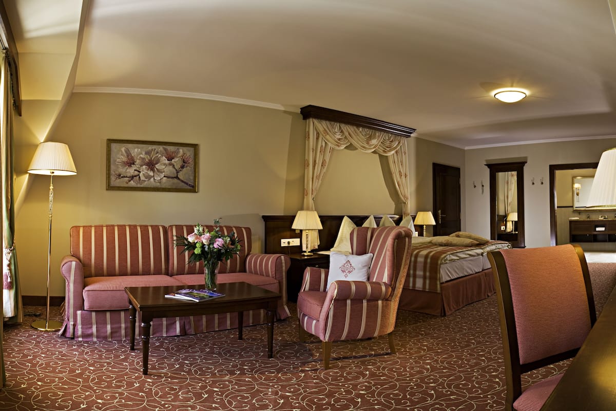 Une chambre d’hôtel comprenant un lit, un canapé, une chaise, une table de chevet, une lampe, un tableau et une moquette.