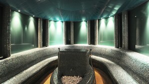 A spa area with mosaic-tiled walls and benches, a central heated stone feature, and recessed lighting. - Grandhotel Lienz (Lienz)