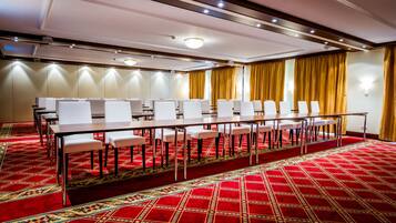 Una sala conferenze con un lungo tavolo e sedie, pavimento rivestito di moquette e tende.