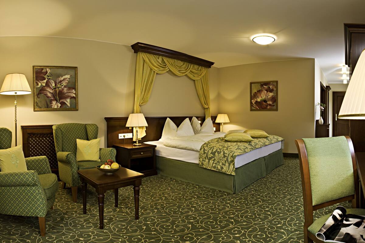 Une chambre d’hôtel avec un grand lit, deux fauteuils, une petite table et une table de chevet.