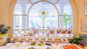 A buffet area with various food items and a view of the dining area through an arched window. - Grandhotel Lienz (Lienz)