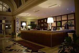 Zona de recepción de un hotel, con mostrador, certificados enmarcados y plantas en macetas.