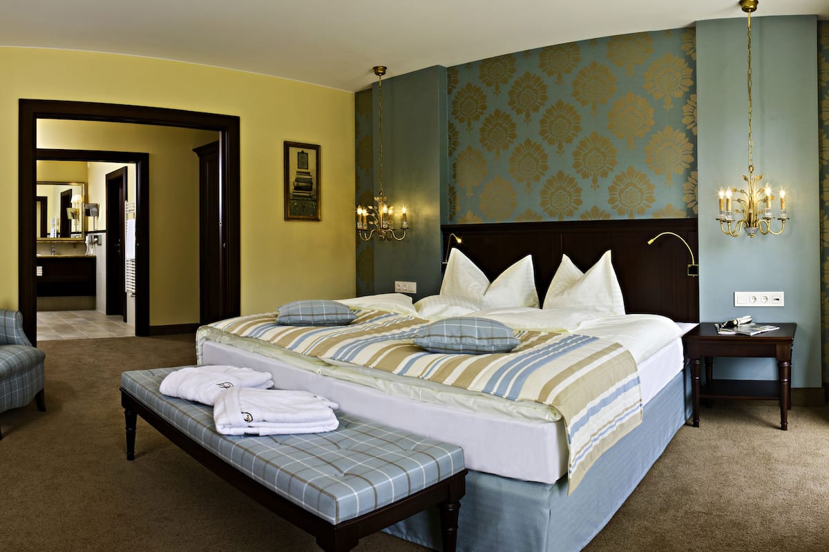 Une chambre d’hôtel avec un grand lit, un banc, une chaise, une table de chevet et un miroir.
