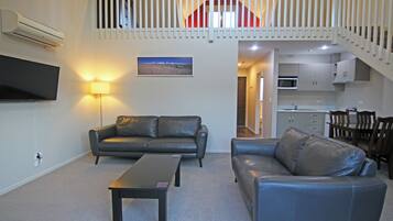 A living room with two leather sofas, a coffee table, a flat-screen TV, and a staircase leading to an upper level.