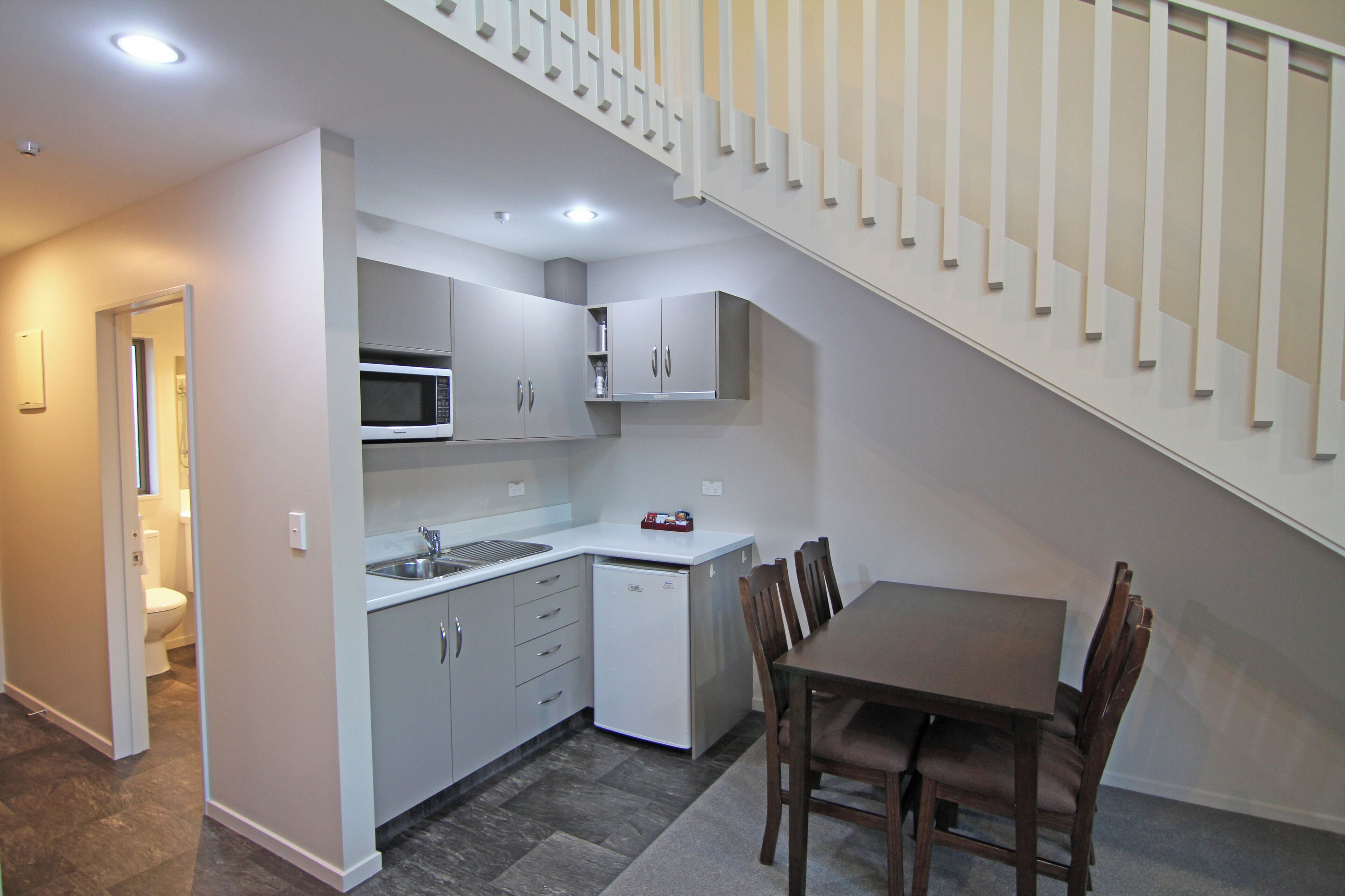Cocina compacta con microondas, fregadero y armarios, una mesa de comedor con sillas y una escalera.