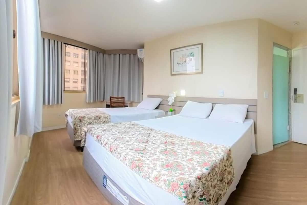 A hotel room with two beds, a window with curtains, a framed picture on the wall, and a door.