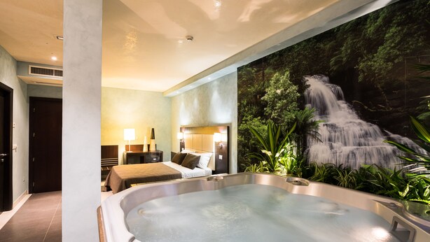 Ett modernt hotellrum med ett stort badkar, en säng med en sänggavel och en väggmålning som föreställer ett vattenfall.
