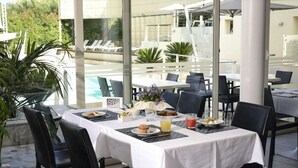 En matplats med bord som är dukade för frukost, med utsikt över en pool och en uteservering.