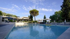 En swimmingpool med solstolar och parasoller, omgiven av byggnader och träd.