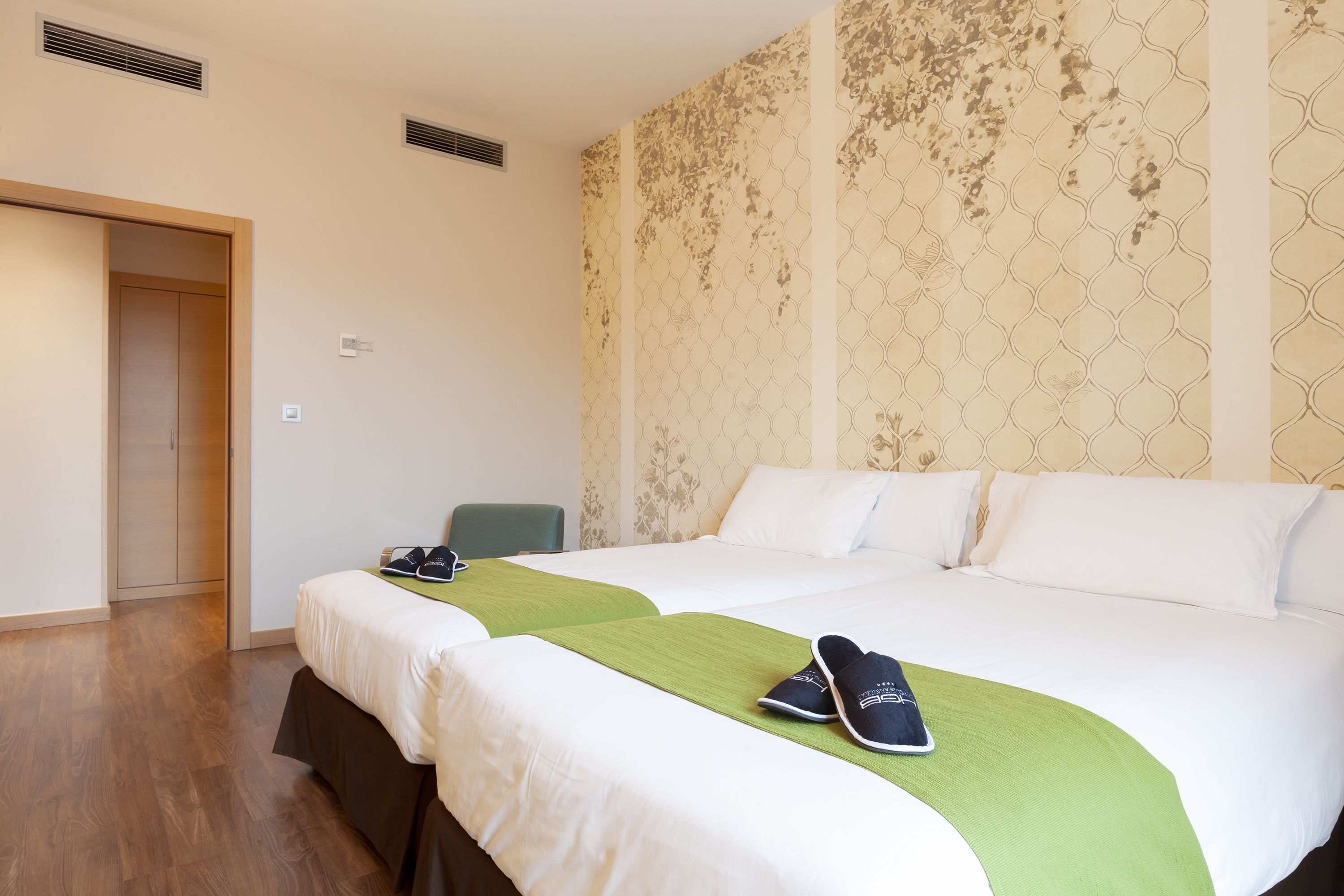 A hotel room with two beds, a green throw blanket, and a pair of shoes on one bed.