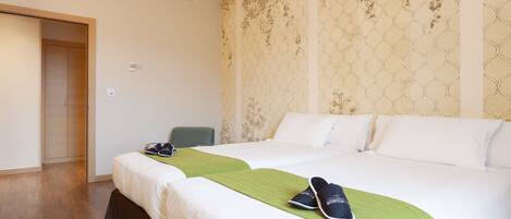 A hotel room with two beds, a green throw blanket, and a pair of shoes on one bed.