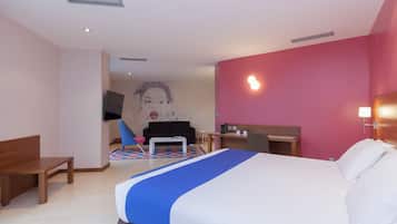 A hotel room with a bed, a desk, a chair, and a television.