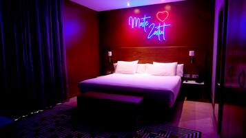 A modern hotel room with a large bed, a neon sign, and a patterned rug.