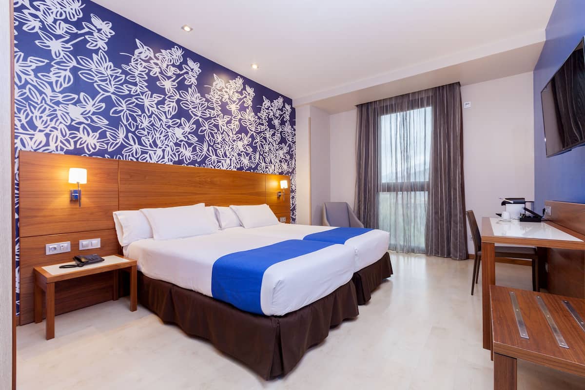 Camera d'albergo con un letto grande, una scrivania, una sedia, un comodino e una parete con un motivo floreale.
