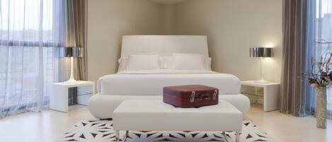 A modern hotel room with a large bed, a bedside table, a nightstand, a decorative rug, and a suitcase on the bed.