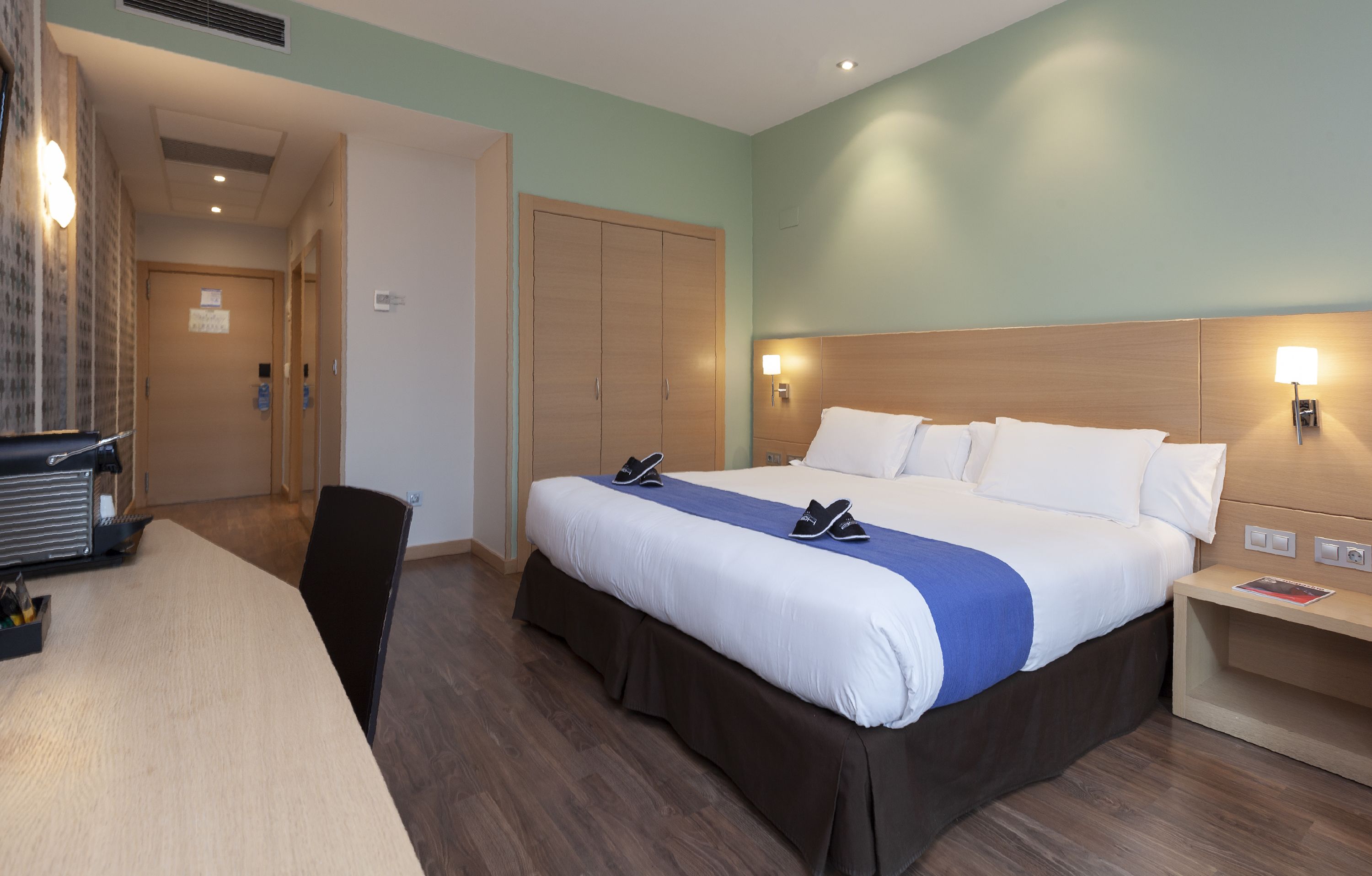 Una habitación de hotel con cama, mesita de noche y escritorio con silla.
